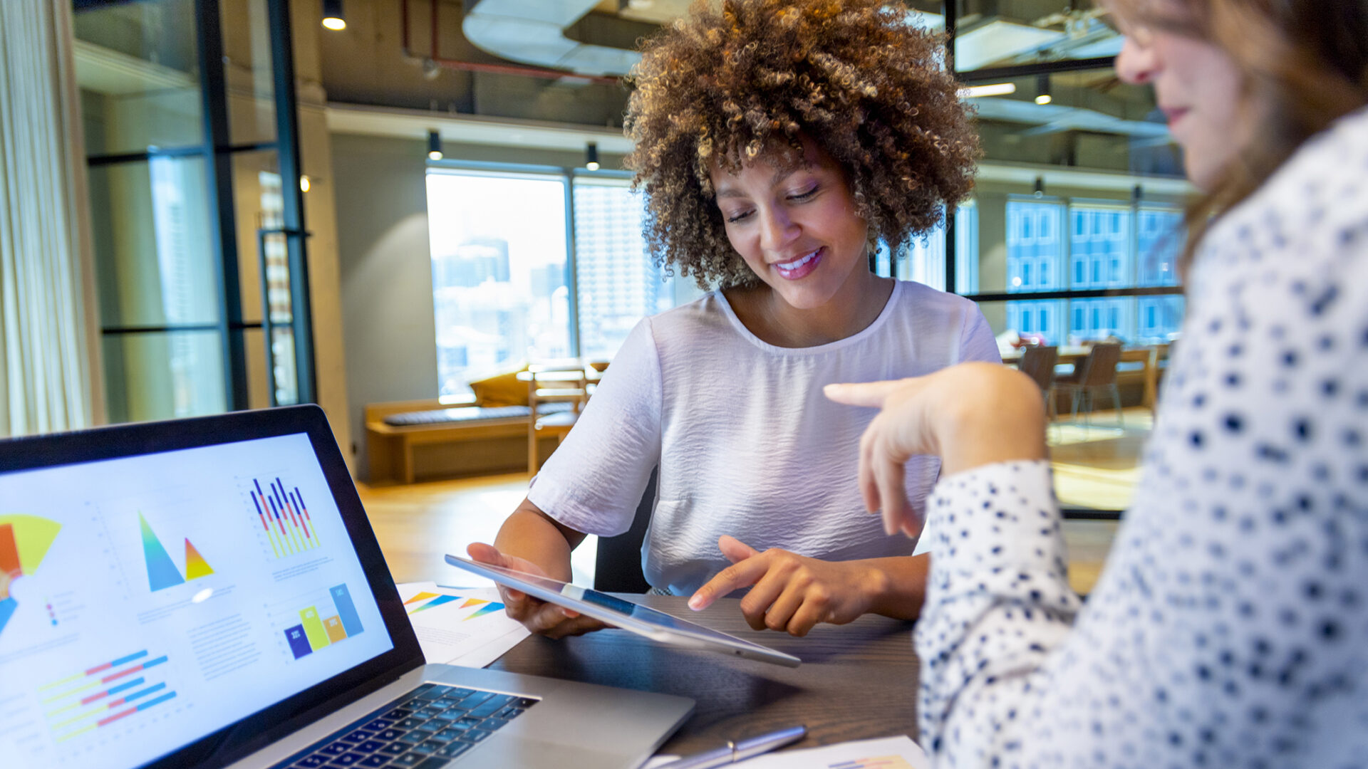 Business colleagues having a conversation. They are discussing finance charts and graphs on a laptop computer. They are both young business people in an office. Could be an interview or consultant working with a client.